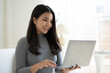 © PaeGAG - Young beautiful Asian woman using laptop computer while sitting on the sofa at her living room.