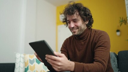 Poster - Young hispanic man using touchpad sitting on sofa at home