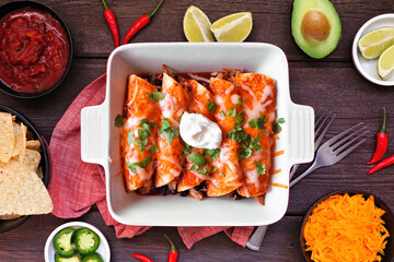 Wall Mural - Chicken enchiladas with black beans. Mexican food dish. Top down flat lay on a dark wood background.