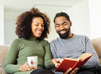 Wall Mural - book woman man reading couple lifestyle young together happy smiling home love happiness caucasian relaxation togetherness sitting beautiful girlfriend boyfriend