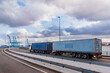 Duo trailer with containers circulating through the entrance bridge to the port of Algeciras for their maritime shipment, with the huge port cranes in the background.