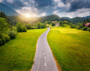 Wall Mural - aerial view of road in green meadows at sunset in summer. top view from drone of rural road, mountai