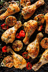 Wall Mural - Spicy roasted chicken legs, drumsticks seasoned with garlic, hot peppers and aromatic herbs on a black background, close-up