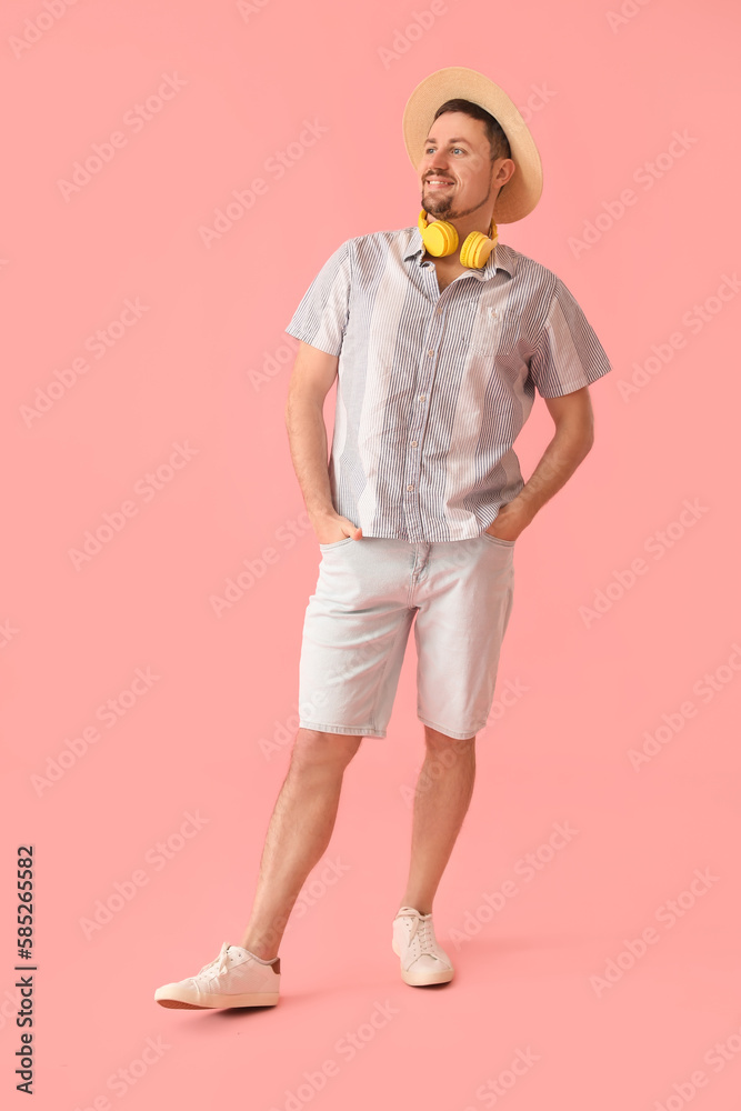 Handsome man in straw hat with headphones on pink background