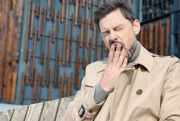 Canvas Print - Sleepy man yawning on wooden bench outdoors. Space for text