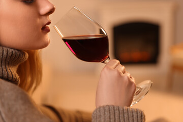 Sticker - Young woman with glass of wine resting near fireplace indoors, closeup