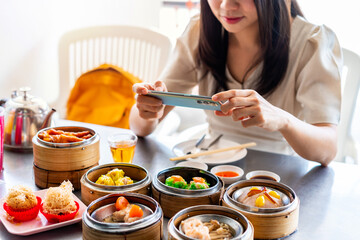 Young woman traveler taking a photo of  traditional Chinese Dim Sum at restaurant while traveling