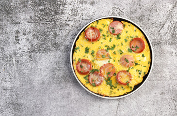 Wall Mural - Omelet with herbs and sausage on a round plate on a dark grey background. Top view, flat lay