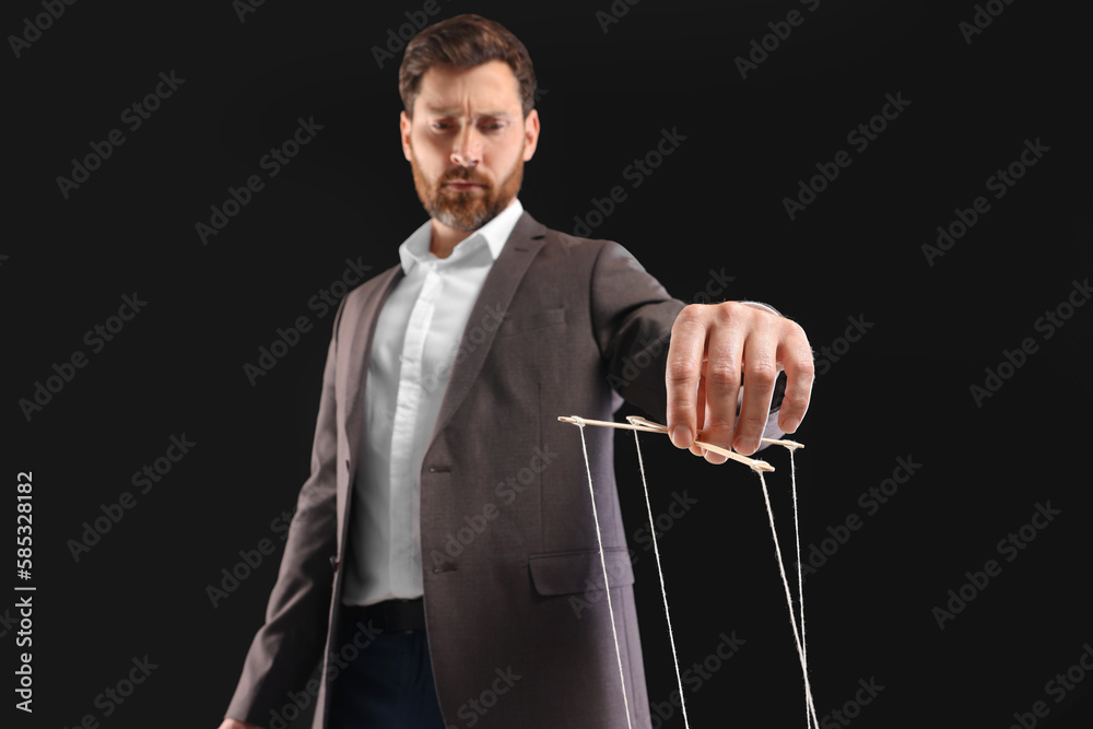 Man in suit pulling strings of puppet on black background, low angle ...