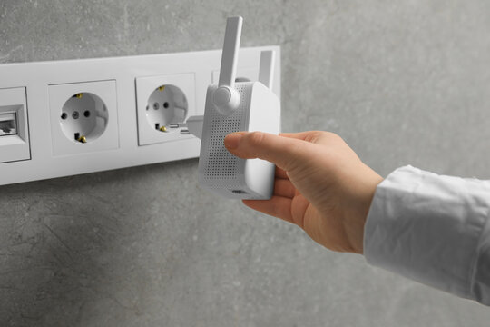 Wall Mural - Woman inserting wireless Wi-Fi repeater into power socket indoors, closeup