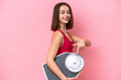 Young Ukrainian woman isolated on pink background holding a weighing machine and pointing it