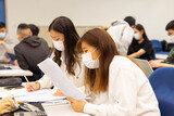 Fototapeta Londyn - group of happy young boys and girls with face mask work, discuss, study on assignment and teaching materials together in classroom in university in Hong Kong during covid-19