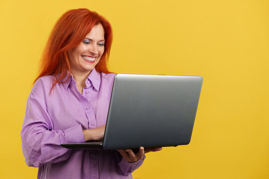Redheaded mature woman smiling while using a laptop