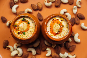 Kulfi ice cream in two clay pots on a solid orange background with cashews and almonds. Kulfi is a popular traditional Indian dessert made of milk with spices and nuts