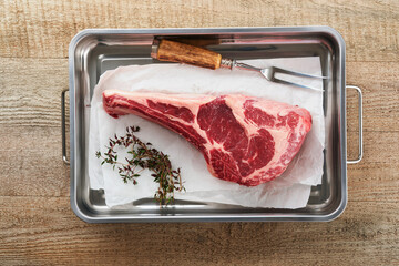 Wall Mural - Fresh tomahawk raw steak. Dry aged raw tomahawk beef steak with herbs and salt on old wooden background. Preparing to grill.  Top view and copy space.