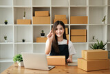 Fototapeta Sport - Young asian woman startup small business freelance pointing finger up with parcel box and computer laptop on table and sitting isolated on green background, Online marketing and delivery concept
