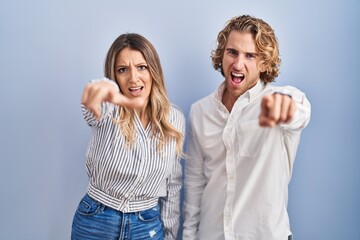 Poster - Young couple standing over blue background pointing displeased and frustrated to the camera, angry and furious with you