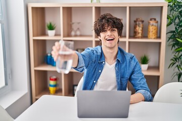 Poster - Young hispanic man using laptop drinking water at home