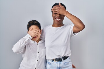 Wall Mural - Young mother and son standing together over white background smiling and laughing with hand on face covering eyes for surprise. blind concept.