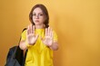 Young caucasian woman wearing student backpack over yellow background moving away hands palms showing refusal and denial with afraid and disgusting expression. stop and forbidden.