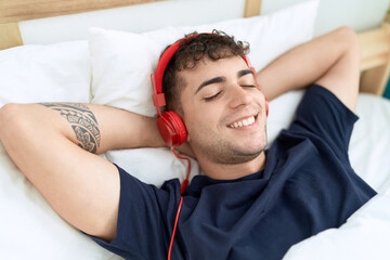 Sticker - Young hispanic man listening to music lying on bed at bedroom