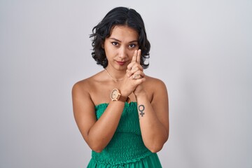 Sticker - Young hispanic woman standing over isolated background holding symbolic gun with hand gesture, playing killing shooting weapons, angry face