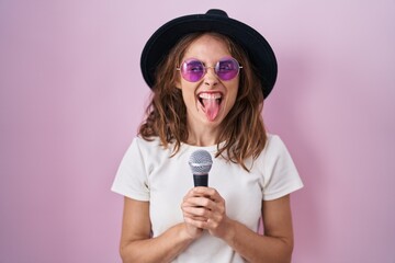 Canvas Print - Beautiful brunette woman singing song using microphone sticking tongue out happy with funny expression.