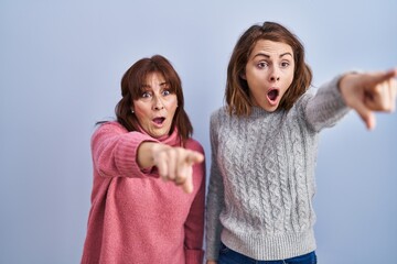 Wall Mural - Mother and daughter standing over blue background pointing with finger surprised ahead, open mouth amazed expression, something on the front