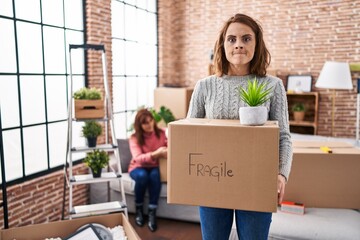 Poster - Mother and daughter moving to a new home holding cardboard box skeptic and nervous, frowning upset because of problem. negative person.