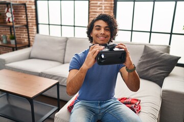 Sticker - Young hispanic man smiling confident holding virtual reality goggles at home