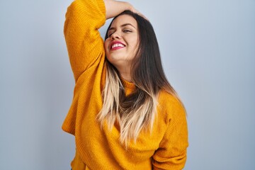 Wall Mural - Young hispanic woman standing over isolated background smiling confident touching hair with hand up gesture, posing attractive and fashionable