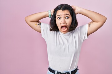 Canvas Print - Young hispanic woman wearing casual white t shirt over pink background crazy and scared with hands on head, afraid and surprised of shock with open mouth