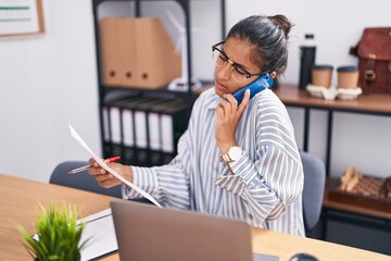 Sticker - Young beautiful hispanic woman business worker talking on smartphone writing on document at office