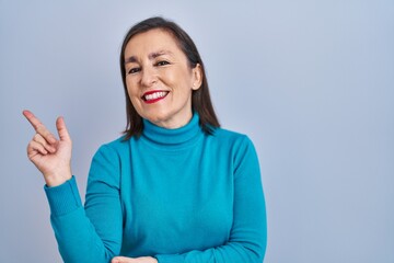 Sticker - Middle age hispanic woman standing over isolated background with a big smile on face, pointing with hand and finger to the side looking at the camera.