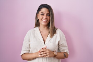 Canvas Print - Blonde woman standing over pink background with hands together and crossed fingers smiling relaxed and cheerful. success and optimistic