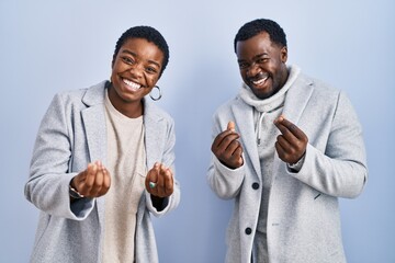 Canvas Print - Young african american couple standing over blue background together doing money gesture with hands, asking for salary payment, millionaire business