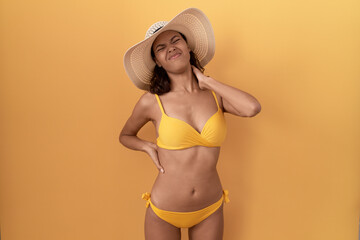 Poster - Young hispanic woman wearing bikini and summer hat suffering of neck ache injury, touching neck with hand, muscular pain