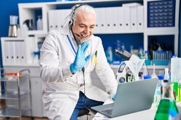 Canvas Print - Middle age man with grey hair working at scientist laboratory doing video call looking positive and happy standing and smiling with a confident smile showing teeth