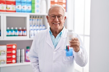 Canvas Print - Senior grey-haired man pharmacist smiling confident holding pills bottle at pharmacy