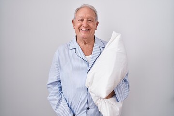 Wall Mural - Senior man with grey hair wearing pijama hugging pillow with a happy and cool smile on face. lucky person.