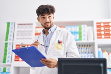 Poster - Young arab man pharmacist smiling confident reading document at pharmacy