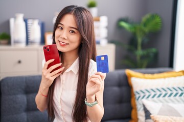 Canvas Print - Young chinese woman using smartphone and credit card sitting on sofa at home