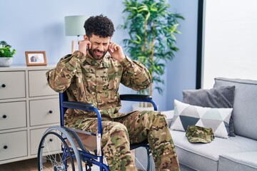 Sticker - Arab man wearing camouflage army uniform sitting on wheelchair covering ears with fingers with annoyed expression for the noise of loud music. deaf concept.