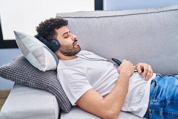 Sticker - Young arab man listening to music sleeping on sofa at home