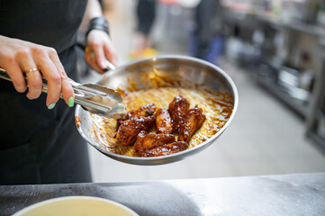 woman chef cooking chicken wings in a sauce in the kitchen