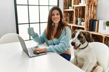 Poster - Young woman using laptop sitting on table with dog at home