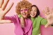 © wayhome.studio - Positive overjoyed women keep arms outstreched laugh happily dressed in green and pink jumpers embrace and foolish around smile gladfully poses indoor. Friendship positive emotions and fun concept