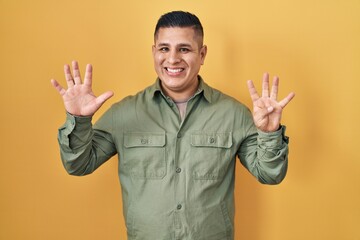 Canvas Print - Hispanic young man standing over yellow background showing and pointing up with fingers number nine while smiling confident and happy.