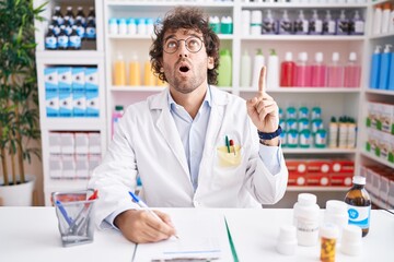 Wall Mural - Hispanic young man working at pharmacy drugstore amazed and surprised looking up and pointing with fingers and raised arms.