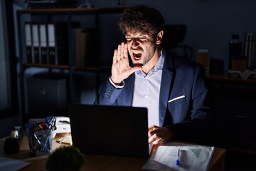 Canvas Print - Hispanic young man working at the office at night shouting and screaming loud to side with hand on mouth. communication concept.